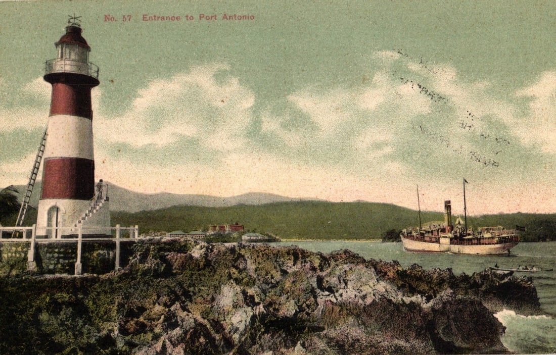 Early 20th Century Lithograph Postcard of Port Antonio, Jamaica: Harbor View with Lighthouse and: A colorized lithograph postcard depicting the entrance to Port Antonio, Jamaica. A prominent red and white striped lighthouse with an external ladder stands on a rocky outcrop in the foreground to the