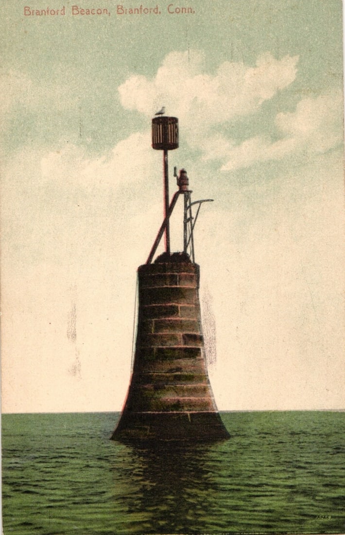 Branford Beacon Coastal Landmark, Branford, Connecticut, circa 1913 postcard: A beacon tower rises from calm green water under a light blue sky with white clouds. A bird is perched atop the structure. The beacon is centrally positioned, tapering upwards from a wide, stone-textu