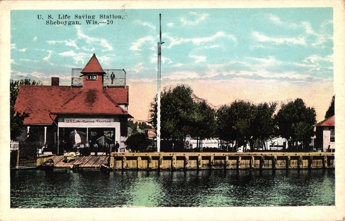 Chromolithograph postcard of U. S. Life Saving Station, Sheboygan, Wisconsin, early 1900s.: A chromolithograph postcard features the U. S. Life Saving Station in Sheboygan, Wisconsin, viewed from across a body of water. The station building has a red-tiled roof and cupola, with two lifeboats