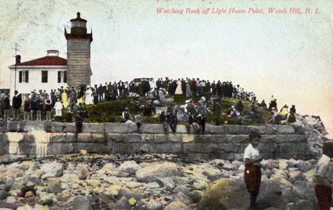 Historic Postcard: Watching Rock off Lighthouse Point, Watch Hill, R.I., with Crowd, Early 20th: A large crowd of people gathers on a rocky outcrop overlooking the sea, with a lighthouse and an adjacent two-story building visible to the left. The lighthouse features a dark lantern room and a whit