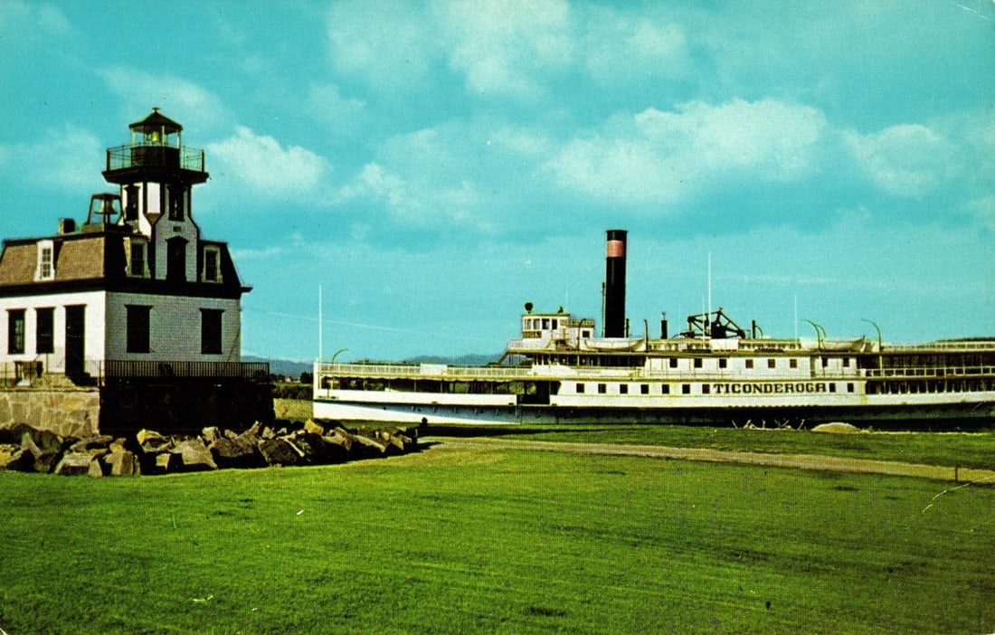 Historic Sidewheeler Ticonderoga with Colchester Reef Lighthouse, Shelburne, Vermont postcard: The sidewheeler TICONDEROGA and the Colchester Reef Lighthouse are depicted in a color photograph. The large, white steamboat, with its red and black smokestack, rests on land. Its name, "TICONDEROGA,