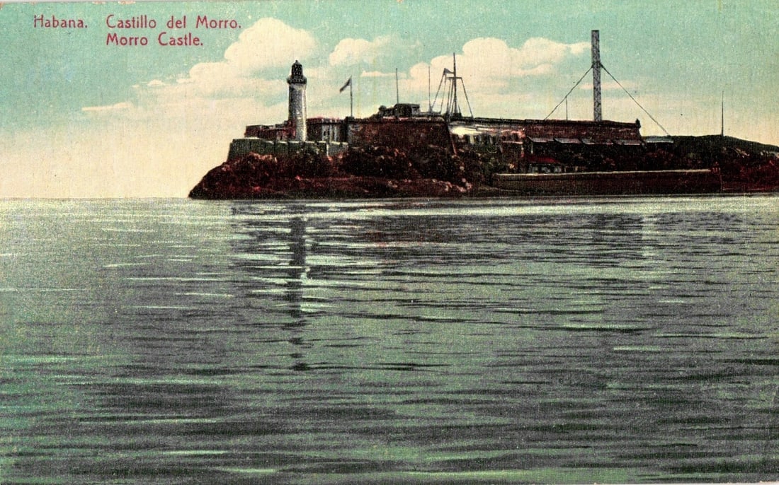 Historic Morro Castle Lighthouse and Fortress, Havana, Cuba, colorized view postcard: Morro Castle, a historic fortress featuring a prominent lighthouse, stands on a rocky outcrop, viewed from the water. The white lighthouse, topped with a dark dome, rises from the left side of the mul