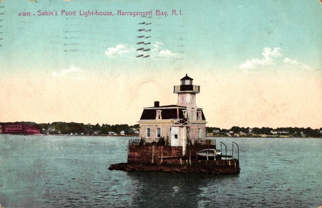 Sabin's Point Lighthouse on Narragansett Bay, Rhode Island, circa 1910s lithograph postcard: A view of Sabin's Point Lighthouse, a white structure comprising a square dwelling base with an attached cylindrical tower topped by a lantern room. The lighthouse is situated on a stone or concrete f