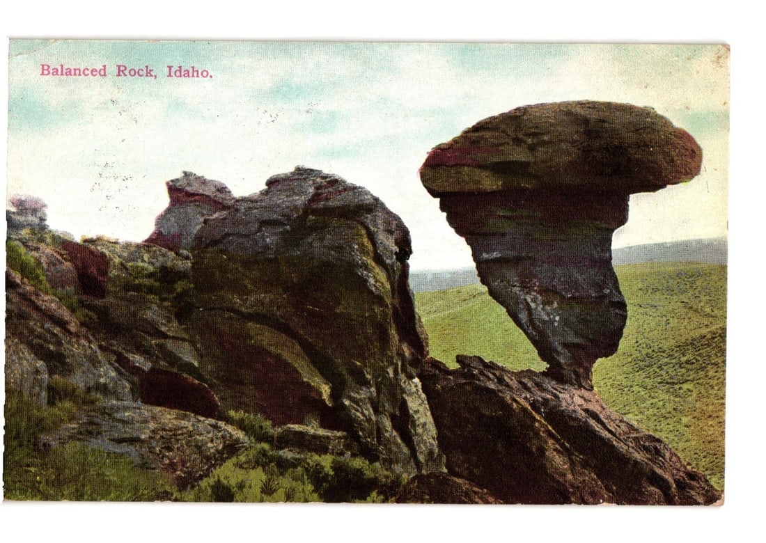 Balanced Rock, Idaho, geological formation view, an early 20th-century American landscape postcard.: A prominent natural rock formation, Balanced Rock, stands on the right, characterized by a large, flat cap balanced on a narrower, columnar base. To the left, a rugged rocky outcrop with varied colora