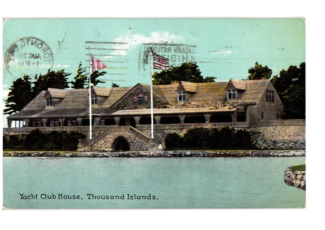 Historic Yacht Club House, Thousand Islands, with flags, circa 1913 chromolithograph postcard.: A grand stone yacht club house with multiple gabled roofs and dormer windows stands prominently on the waterfront. The building features a large stone archway at its base and covered verandas along it