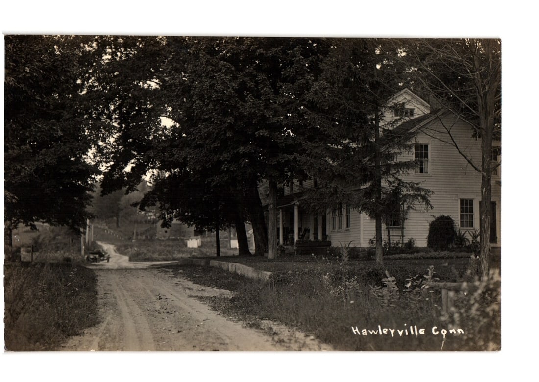 Hawleyville, Connecticut Rural Landscape: Dirt Road, Large House, & Trees Real Photo postcard: A large, two-story wooden house with multiple windows and dark trim stands prominently on the right side of the frame, partially obscured by dense, mature trees. The trees dominate the left and center