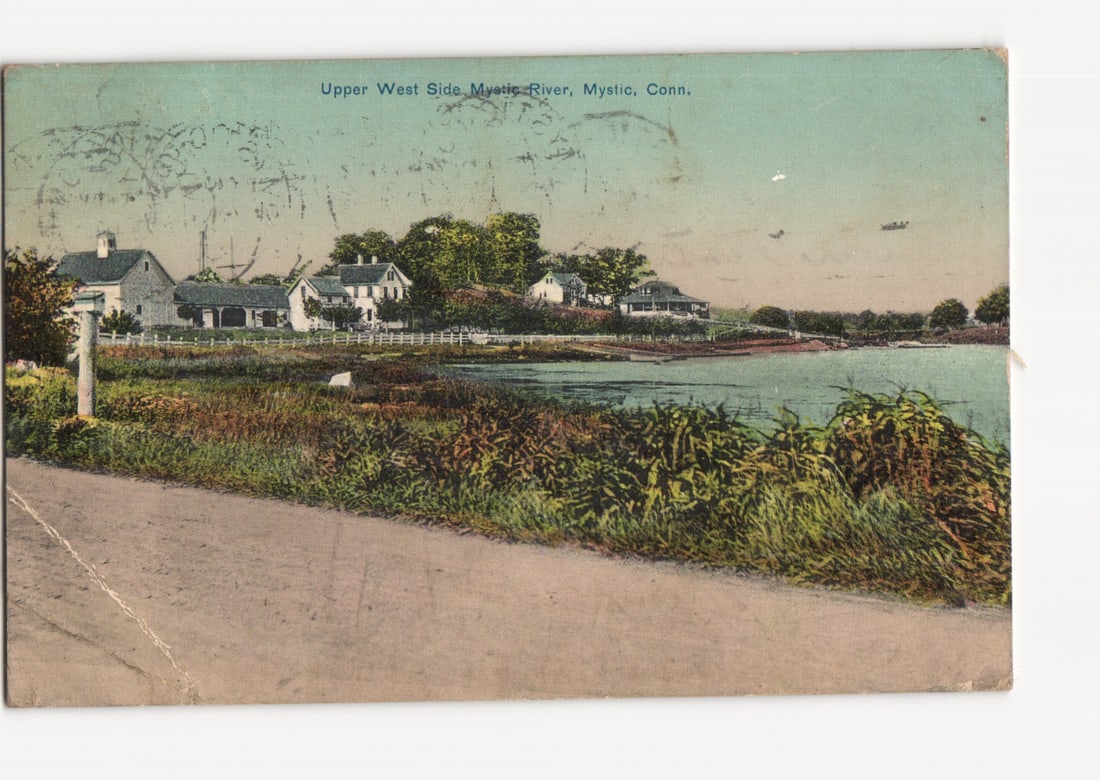 Early 20th-century postcard featuring the Upper West Side of Mystic River, Mystic, Connecticut: A scenic view of the Upper West Side of the Mystic River in Mystic, Connecticut. A calm body of water occupies the middle and right portions of the image. The foreground features a dirt road or path s