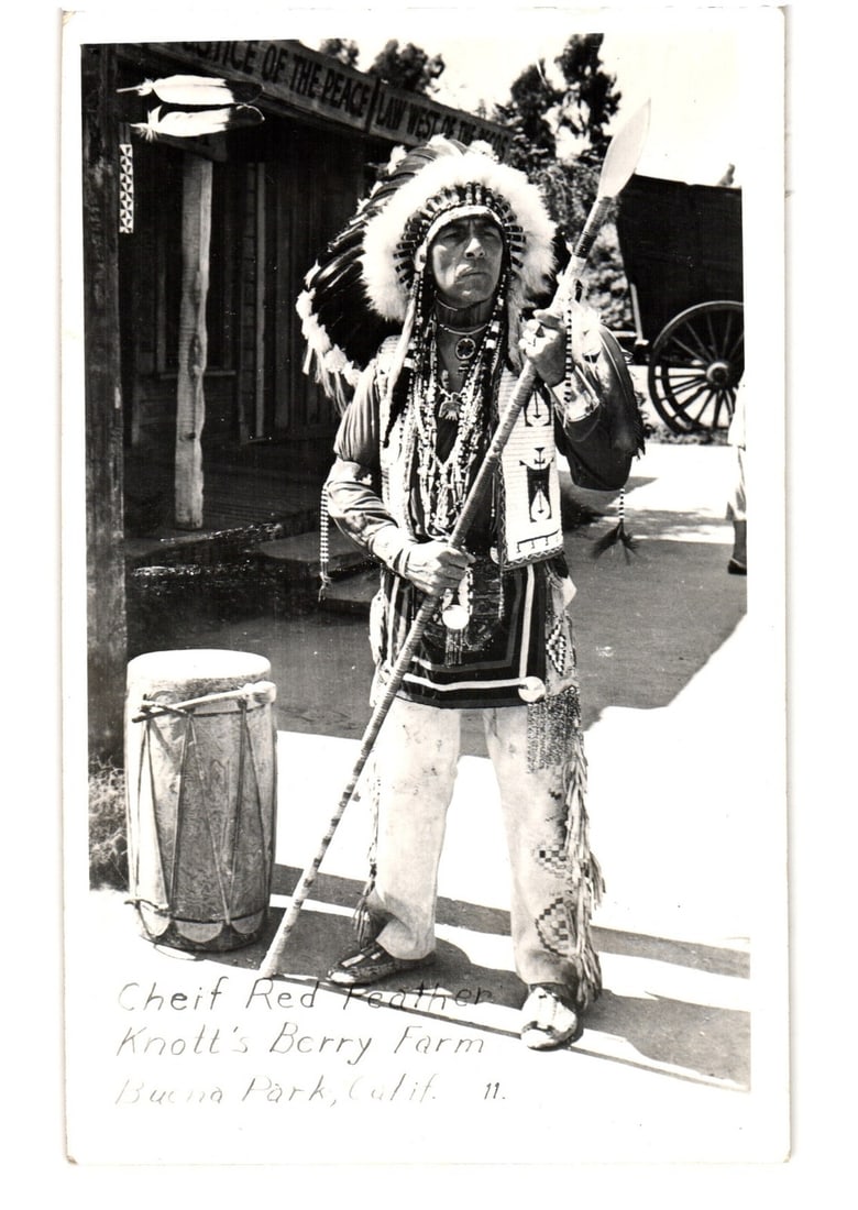 Chief Red Feather at Knott's Berry Farm Ghost Town, Buena Park, California postcard, 1953: A full-length photographic portrait of a man identified as Chief Red Feather, standing outdoors in what appears to be a recreated Old West or "Ghost Town" setting. He is dressed in elaborate Native Am