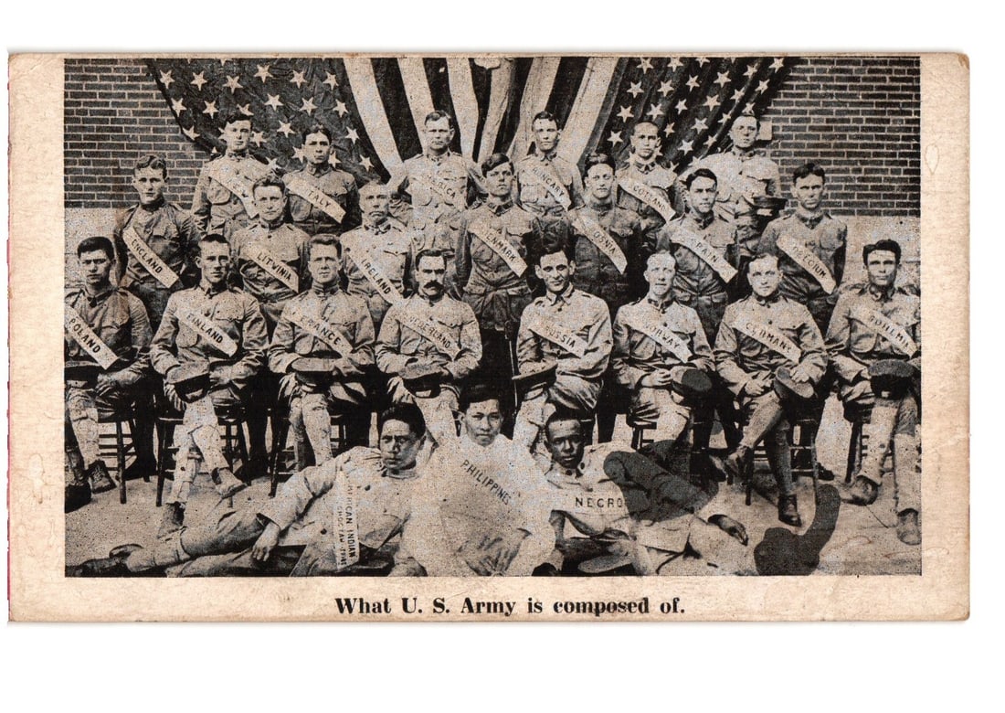 Early 20th-century U.S. Army soldiers group portrait postcard with national sashes on flag: A group portrait features twenty-six men in military uniforms, arranged in three rows: seated, standing, and reclining. A large United States flag forms the backdrop. Each man wears a sash across his 