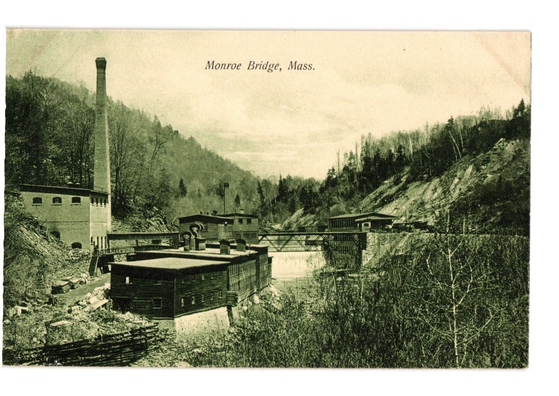 Monroe Bridge, Massachusetts Industrial Valley Landscape with Mill Complex postcard: A monochromatic image depicts an industrial complex situated within a valley. A tall, tapering smokestack rises above a multi-story brick building on the left. In the midground, several wooden structu