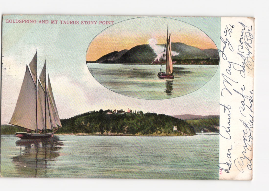Scenic postcard of Goldspring, Mount Taurus, and Stony Point, featuring sailboats.: A gaff-rigged sailboat with two masts, sails furled, is prominent in the foreground of a body of water, reflecting on its surface. In the midground, a tree-covered island features structures on its cr