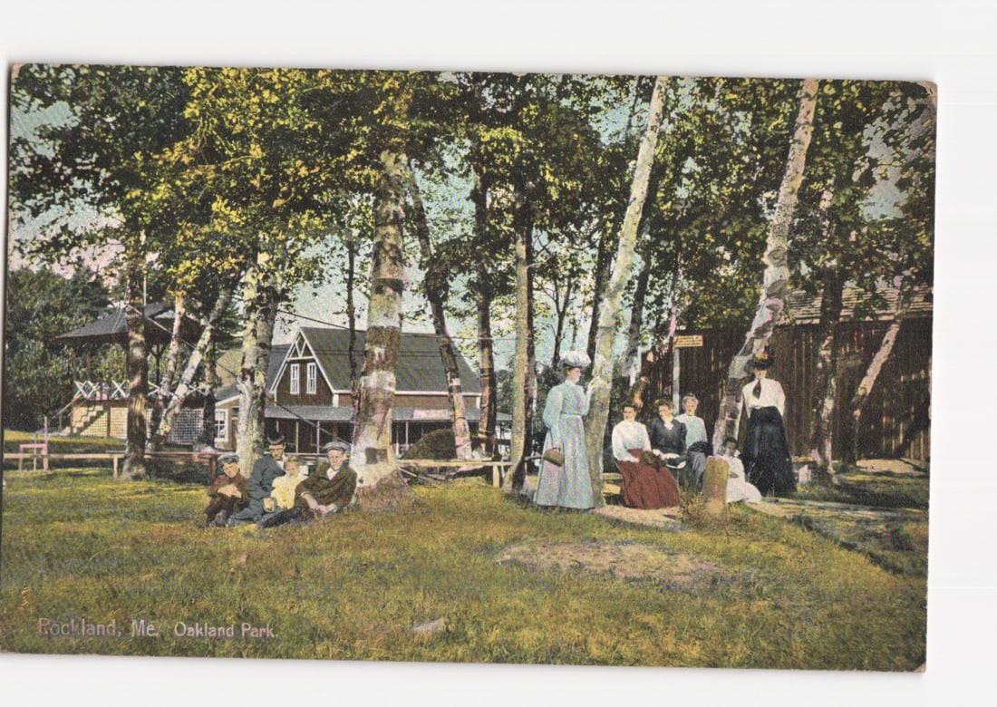 Oakland Park, Rockland, Maine, featuring group of people under trees, early 20th-century postcard.: A group of adults and children are gathered in a park-like setting under a grove of birch trees. Several women are seated or standing, dressed in long skirts and blouses, while men and children are al