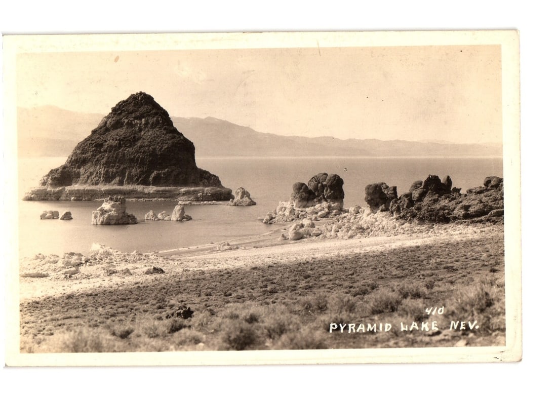 Historic Pyramid Lake, Nevada, landscape postcard featuring unique volcanic formations: A wide-angle, sepia-toned Real Photo Postcard depicts Pyramid Lake, Nevada. A prominent, dark, pyramid-shaped island dominates the left-midground, surrounded by calm water. Several smaller rock format