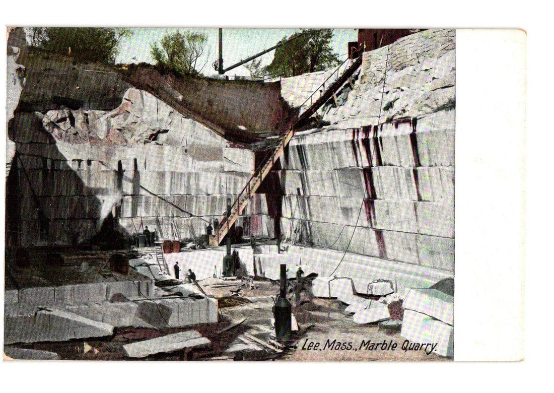 Historic Postcard: Lee, Massachusetts Marble Quarry Operations with Workers and Machinery: A vast open-pit marble quarry is depicted, showing multiple carved levels and large blocks of extracted stone. A long wooden ramp or staircase extends from the quarry floor to the upper edge. Several 