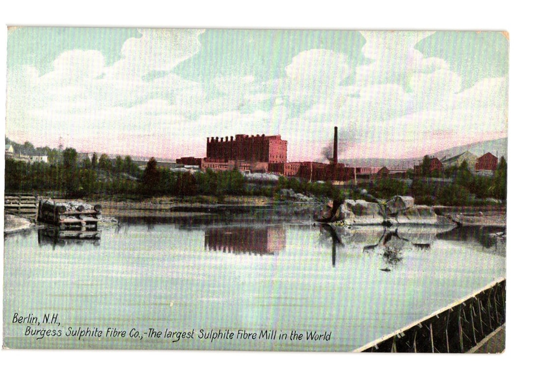 Burgess Sulphite Fibre Co., Berlin, N.H., Largest Sulphite Fibre Mill in the World postcard: An industrial landscape view of the Burgess Sulphite Fibre Co. in Berlin, New Hampshire. The extensive mill complex, featuring multi-story brick buildings and a prominent smokestack emitting smoke, st