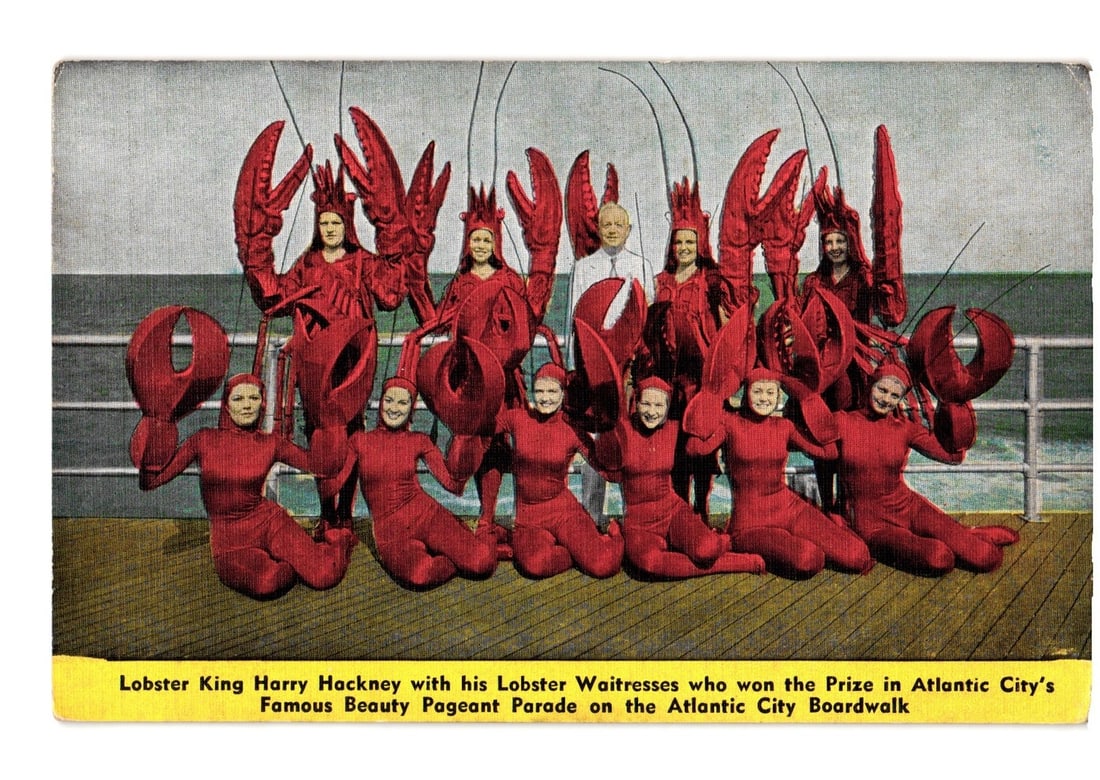 Atlantic City Boardwalk postcard: Harry Hackney with his award-winning Lobster Waitresses: Ten individuals, comprising one man and nine women, are depicted posing on what appears to be a ship deck or pier. Six women are adorned in elaborate red lobster costumes, complete with large claws. T