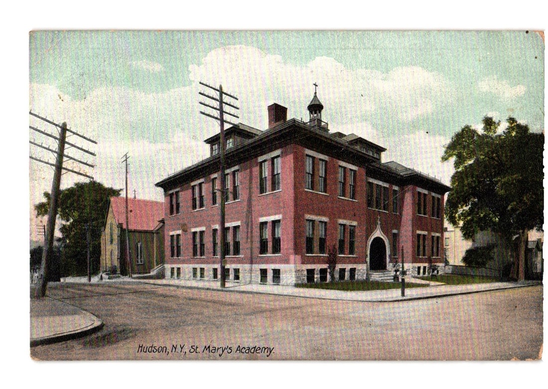 St. Mary's Academy, Hudson, New York - Early 20th Century Architectural Postcard, c. 1911: St. Mary's Academy, a large brick building, is depicted at a street intersection under a partly cloudy sky. The three-story structure features numerous windows, a prominent arched entrance, and a smal