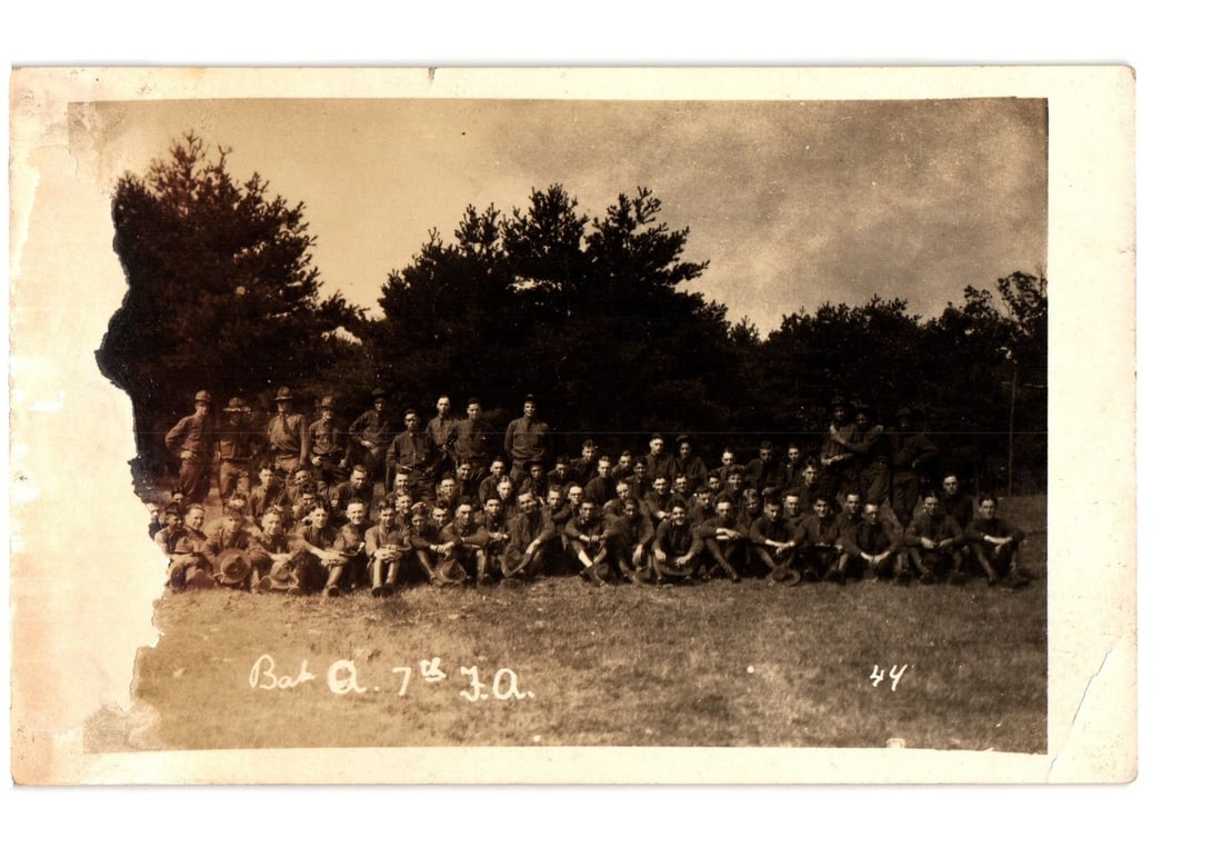 Large Group Portrait of Soldiers, Battery A, 7th Field Artillery, Early 20th Century Postcard.: A large group portrait featuring approximately 50 to 60 soldiers in military uniforms, posed outdoors on a grassy field. Several soldiers stand in the back row, while the majority are seated cross-leg