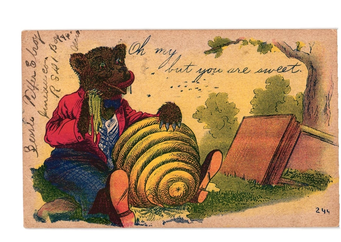 Anthropomorphic Bear Eating Honey from Beehive Chromolithograph Postcard, Elroy, Wisconsin, 1907: An anthropomorphic bear, depicted wearing a red jacket, white shirt, blue striped tie, blue trousers, and orange shoes, is seated beside a large yellow beehive. The bear's right paw is inserted into t