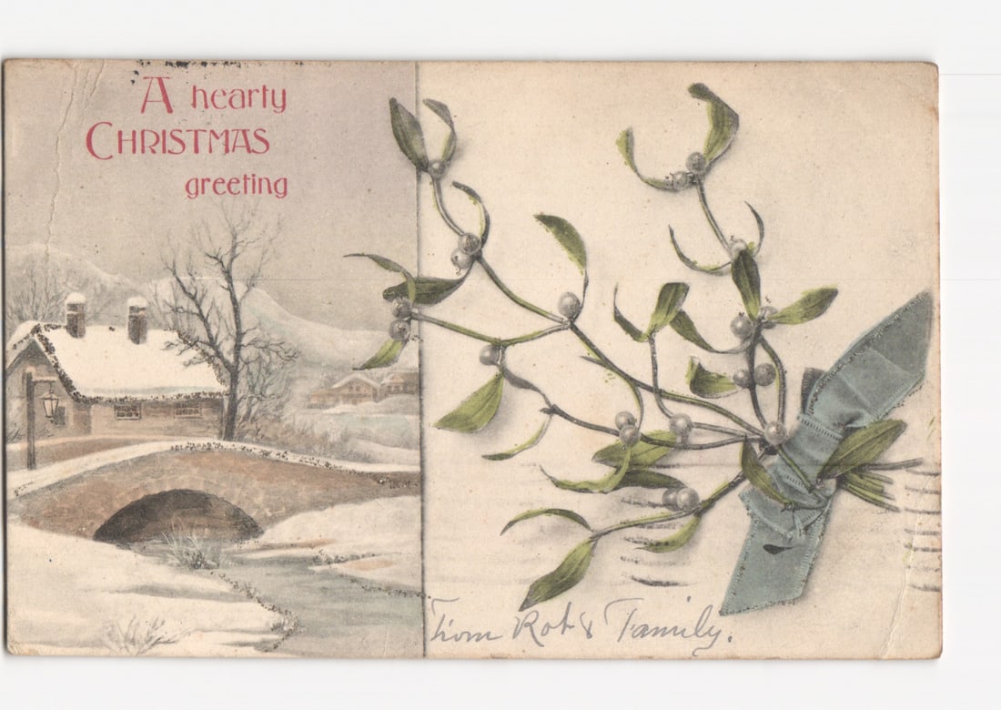 Early 20th Century Chromolithograph Christmas postcard: Snowy village scene with mistletoe, 1906.: A winter landscape scene with a snow-covered cottage, a bare tree, and a stone arch bridge over a stream, with mountains in the background. To the right, a sprig of mistletoe with white berries is tie