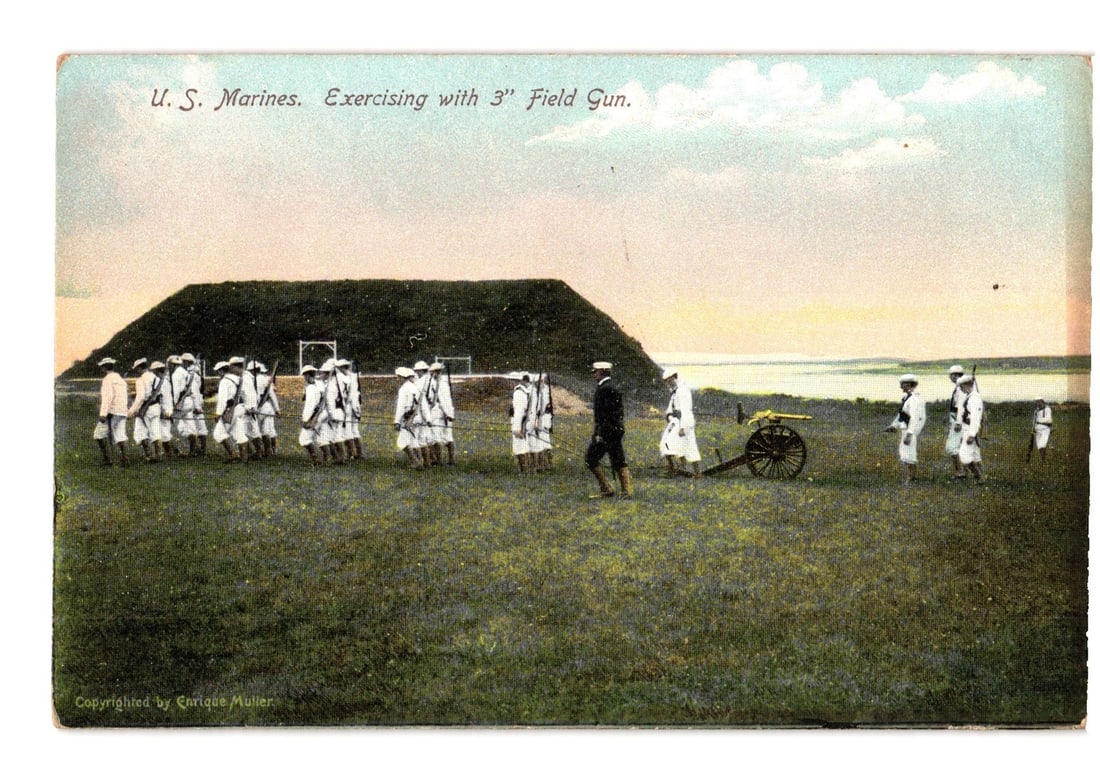 U.S. Marines Exercising with 3-inch Field Gun on Grassy Field Near Water, Early 1900s postcard: A group of U.S. Marines in white uniforms and one officer in a dark uniform are depicted on a large grassy field, engaged in an exercise with a 3-inch field gun. In the background, a prominent dark, s