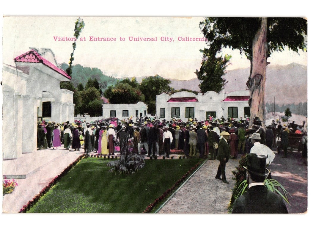 Visitors Gather at Entrance to Universal City, California, Early 20th Century Postcard: A large crowd of people is depicted gathered at the entrance of Universal City, California. Several white buildings with red tile roofs are visible, featuring columns and arches. The crowd occupies a 
