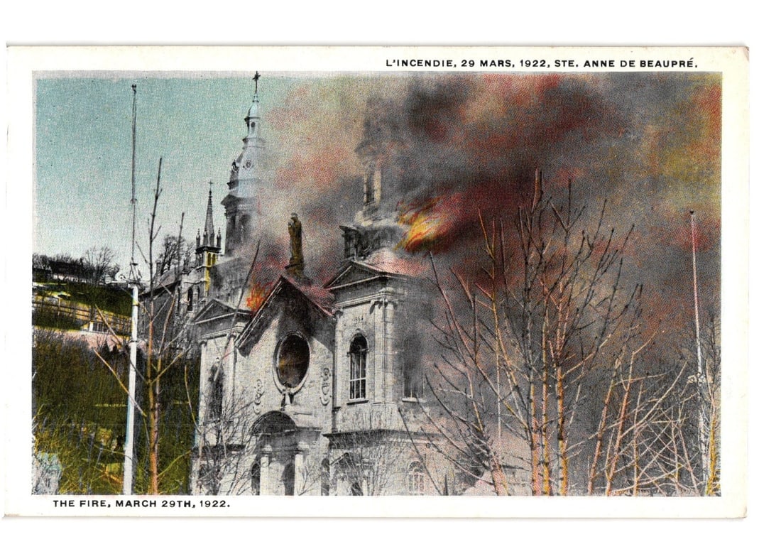Ste. Anne de Beaupre Church on fire, March 29, 1922, a documented event postcard.: A church building is depicted actively on fire, with thick smoke and flames visible from the upper sections, including the dome and roof. The structure exhibits classical architectural details, such a