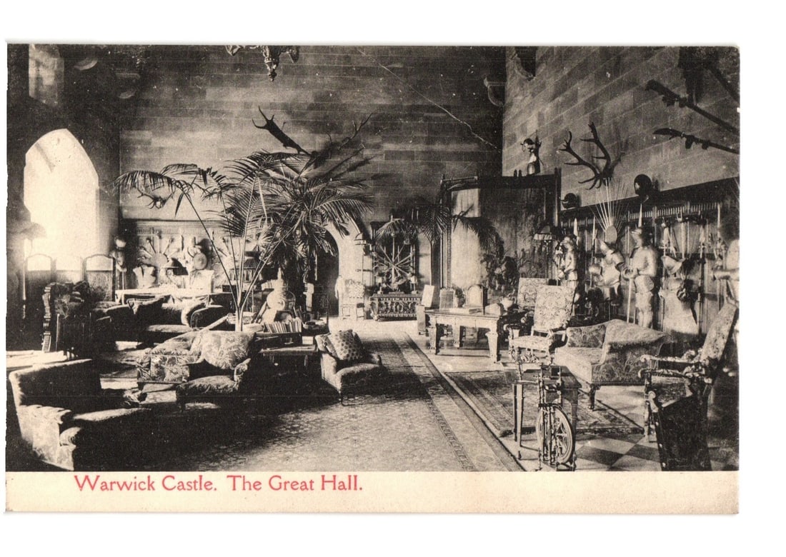 Detailed Interior View of Warwick Castle's Great Hall, England, Early 20th Century Postcard: An interior view of Warwick Castle's Great Hall. The expansive room is furnished with numerous upholstered sofas and armchairs in patterned fabrics, arranged throughout the space. Large potted palm tr