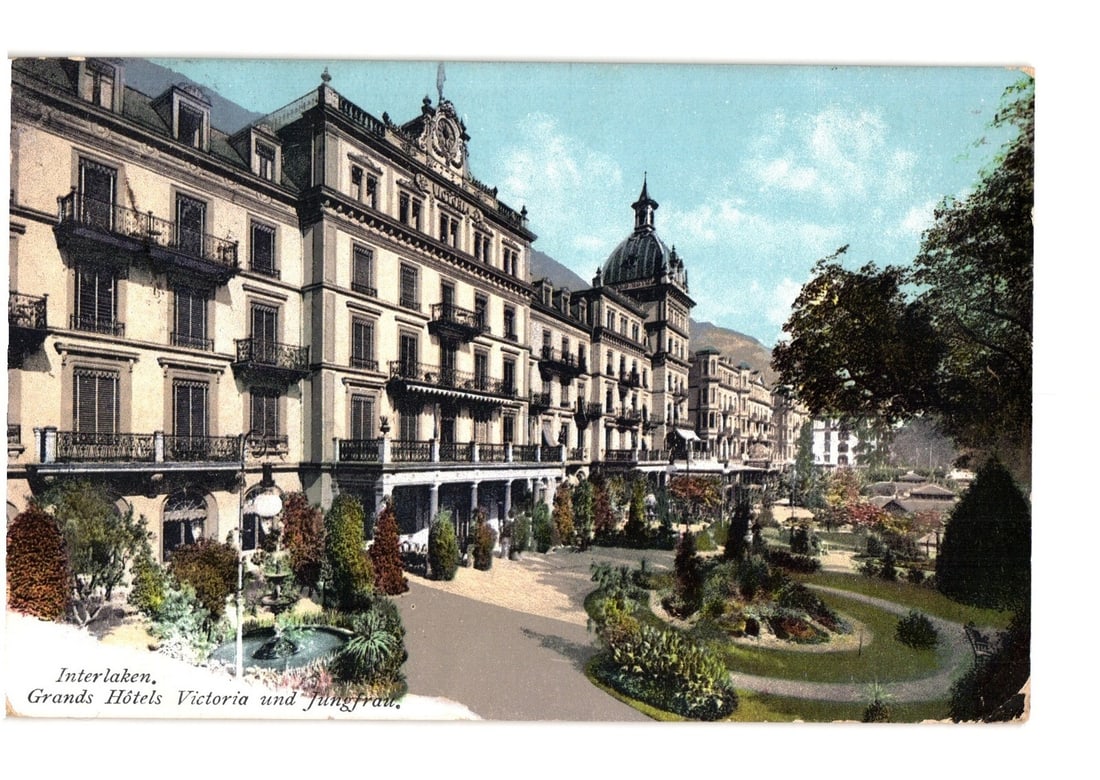 Ornate Grand Hotels Victoria and Jungfrau, Interlaken, Switzerland, circa 1910 postcard view: A grand multi-story hotel complex, the Grand Hotels Victoria und Jungfrau, is depicted from a low vantage point. The elaborate building features multiple balconies, ornate architectural details, and a