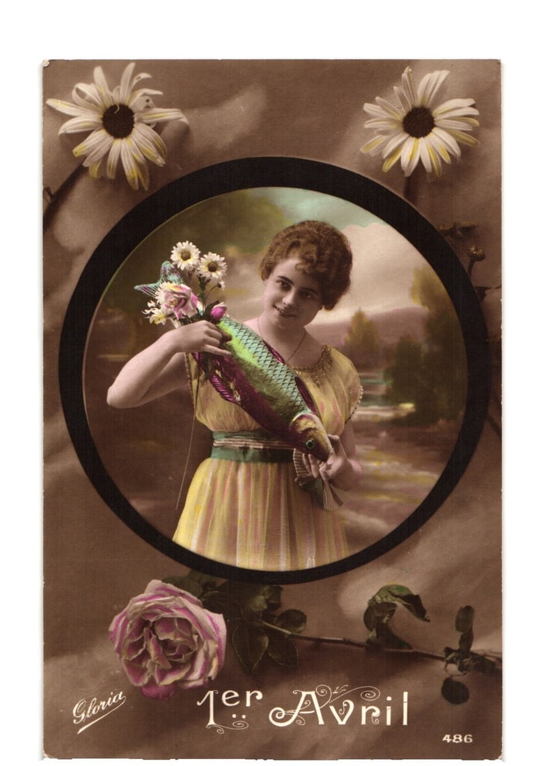 Vintage French April Fool's Day postcard featuring a young woman holding a brightly colored fish.: A young woman, smiling, is featured within a circular inset photograph, centrally positioned on the postcard. She has curly hair and wears a light-colored dress with a green sash. In her left arm, she