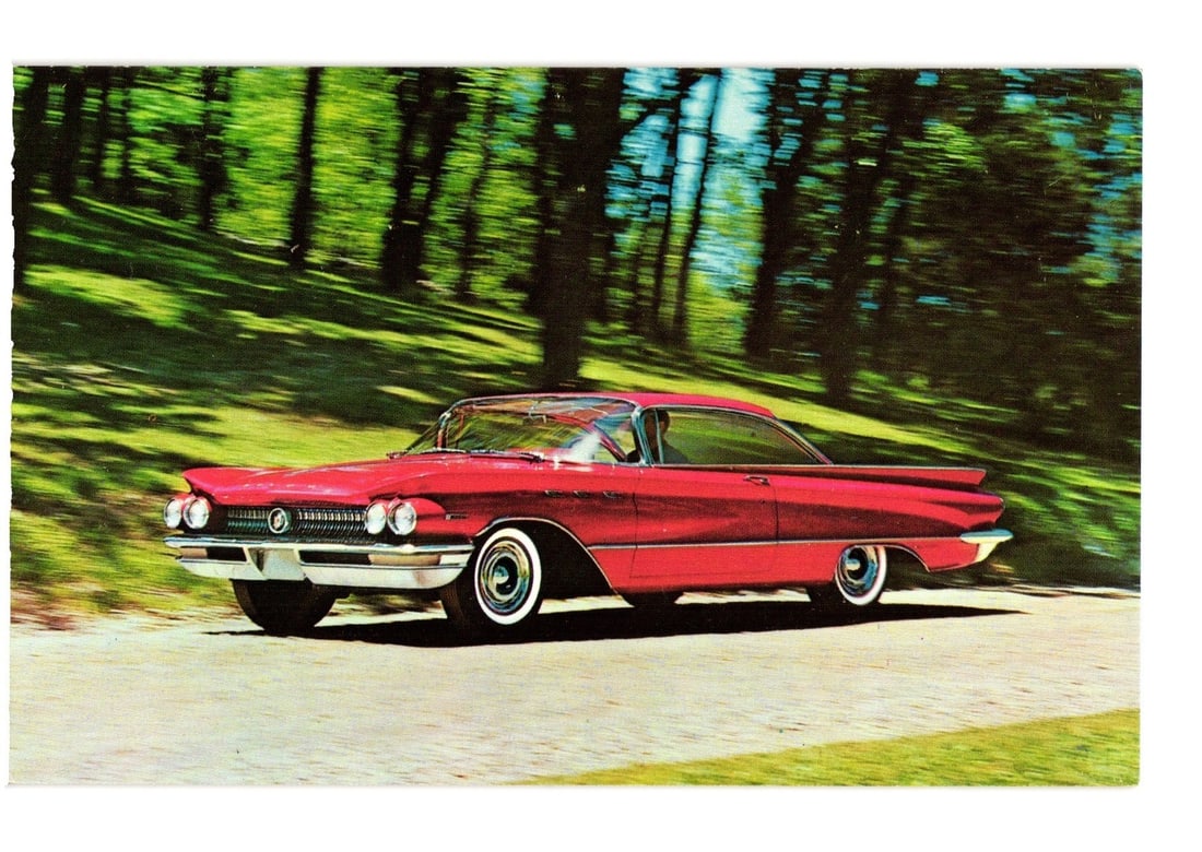 Turbine Drive Buick Invicta 2-Door Hardtop, Magic-Mirror Titian Red, circa 1960 postcard: A glossy red Buick Invicta 2-Door Hardtop automobile is depicted in motion on a paved road. The car, featuring prominent chrome trim, white sidewall tires, and distinctive tail fins, is angled towards