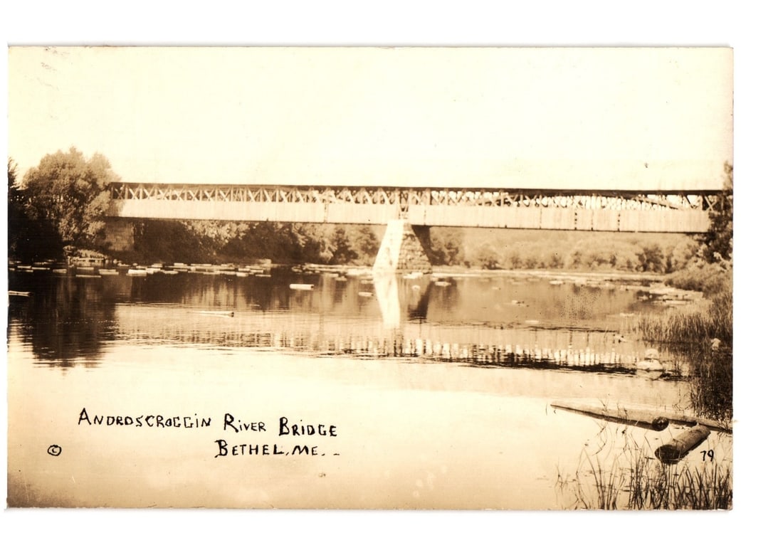 Androscoggin River Bridge, Bethel, Maine, Early 20th Century Sepia Toned Photographic postcard: A sepia-toned photographic view presents the Androscoggin River Bridge in Bethel, Maine. The wooden truss bridge extends across the river, with its structure and surrounding trees clearly reflected in