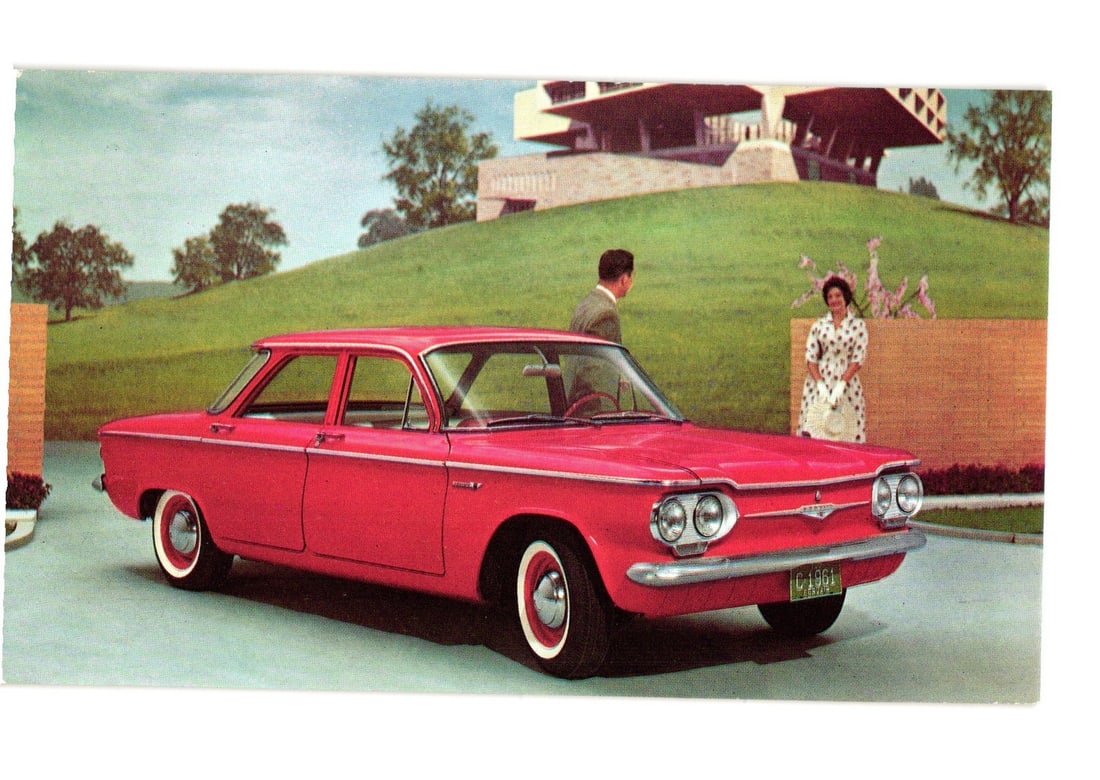 1961 Chevrolet Corvair '700' 4-Door Sedan Promotional Postcard, Couple by Modern Building: A bright red 1961 Chevrolet Corvair "700" 4-Door Sedan is depicted in the foreground, parked on a paved surface. Two individuals, a man and a woman, stand behind the vehicle. The man is positioned to 