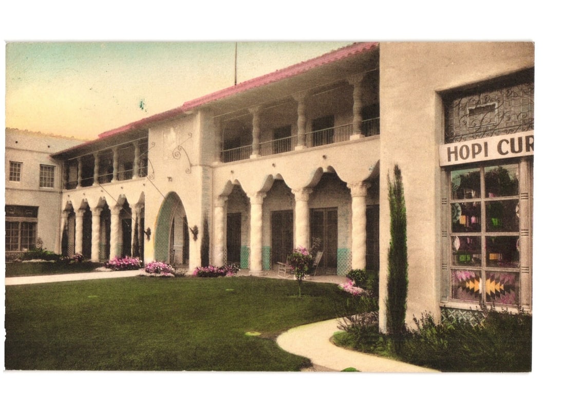 Hand-colored postcard: El Portal Hotel, Mesa, Arizona, with distinct Spanish Colonial architecture.: The El Portal Hotel in Mesa, Arizona, is depicted in a hand-colored photograph. The two-story building features light-colored stucco, a red-tiled roof, and numerous arched openings supported by column