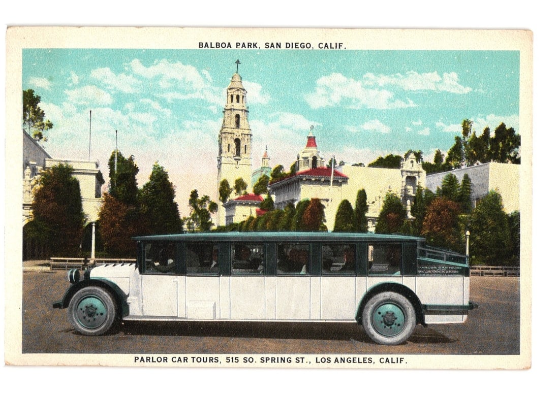 Early 20th Century Parlor Car Tours Bus in Balboa Park, San Diego, California postcard: A long, white and dark green parlor car bus is depicted in a side profile, parked on a paved surface. The bus features multiple windows. In the background, a complex of Spanish Colonial Revival style 