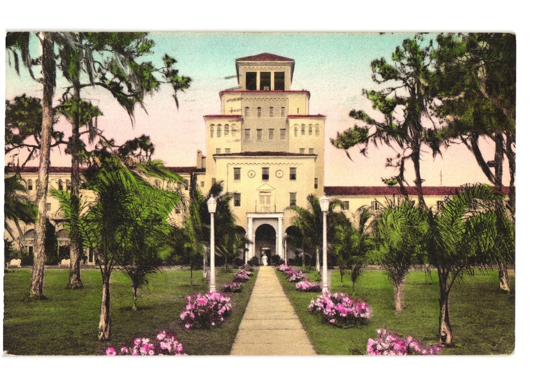 Harder Hall Grand Hotel in Sebring, Florida Hand-Colored Architectural Postcard, Early 20th Century: Harder Hall, a multi-story hotel with central tower and red-tiled roof, stands centrally. A paved pathway leads to its arched entrance, flanked by lawns, pink flower beds, and white lampposts. Palm an