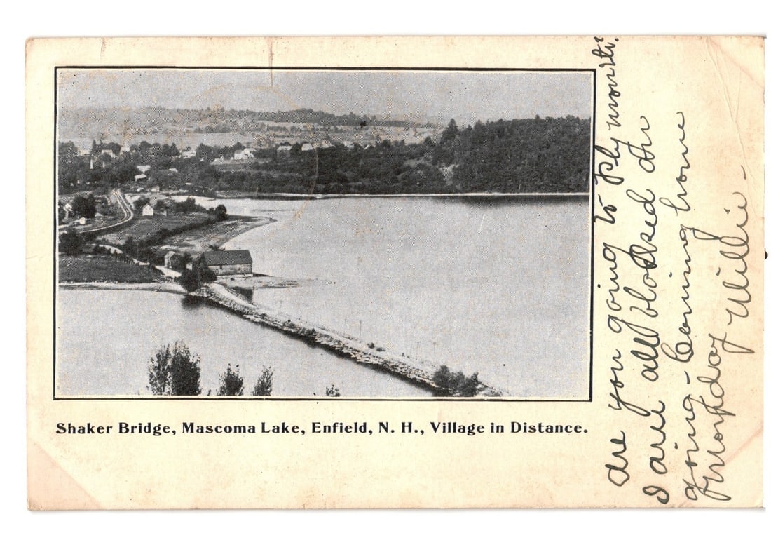 Early 20th Century Postcard: Shaker Bridge, Mascoma Lake, Enfield, New Hampshire Village: A black and white photographic postcard depicting Shaker Bridge extending into Mascoma Lake in Enfield, New Hampshire. A village is visible in the distance along the lake's far shore, backed by forest