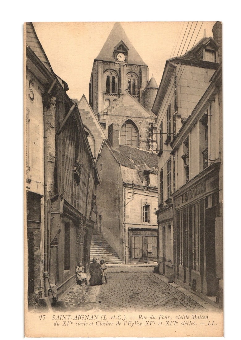 Saint-Aignan, Rue du Four, Old Houses & Church Tower (11th-16th c.) French Real Photo Postcard: A sepia-toned photographic postcard depicts a narrow, cobbled street named Rue du Four in Saint-Aignan, France. The perspective leads towards a prominent church tower, identified as dating from the 11