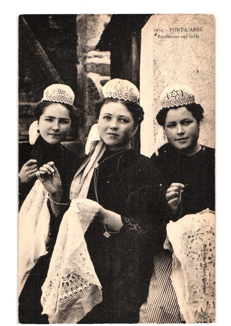 Three women embroidering lace in traditional attire, Pont-l'Abbé, France, photographic postcard.: Three women in traditional attire are depicted from the waist up, engaged in embroidery or lacemaking. Each woman wears a dark blouse and a distinctive, intricately patterned white lace cap. They hold