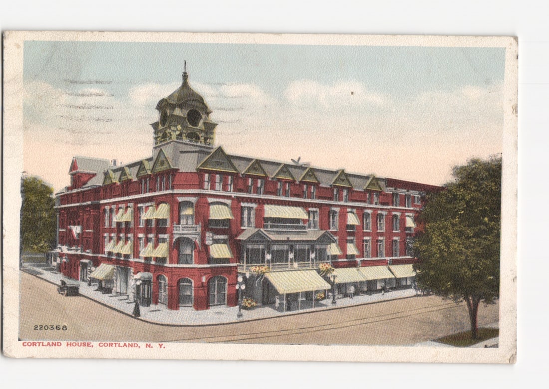 Cortland House Hotel, a grand brick edifice in Cortland, N.Y. in this 1920 postcard.: A large, multi-story brick hotel, the Cortland House, stands prominently at a street intersection. The building features a red brick facade, numerous windows with light-colored awnings, and white trim