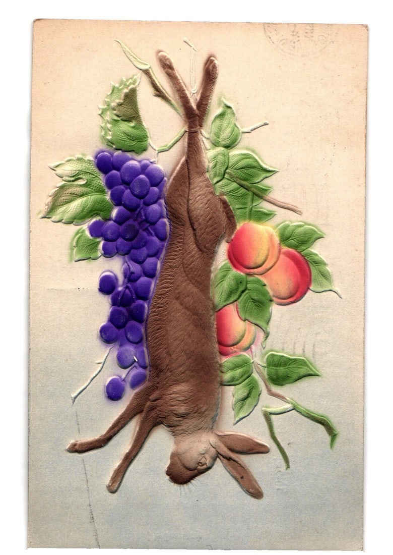 Embossed hunting trophy postcard featuring a hanging rabbit, grapes, and peaches, circa 1900s.: A colorized lithograph with heavy embossing depicting a still life composition. A brown rabbit is suspended vertically by its hind legs, head downwards, positioned centrally. To the left, a cluster of