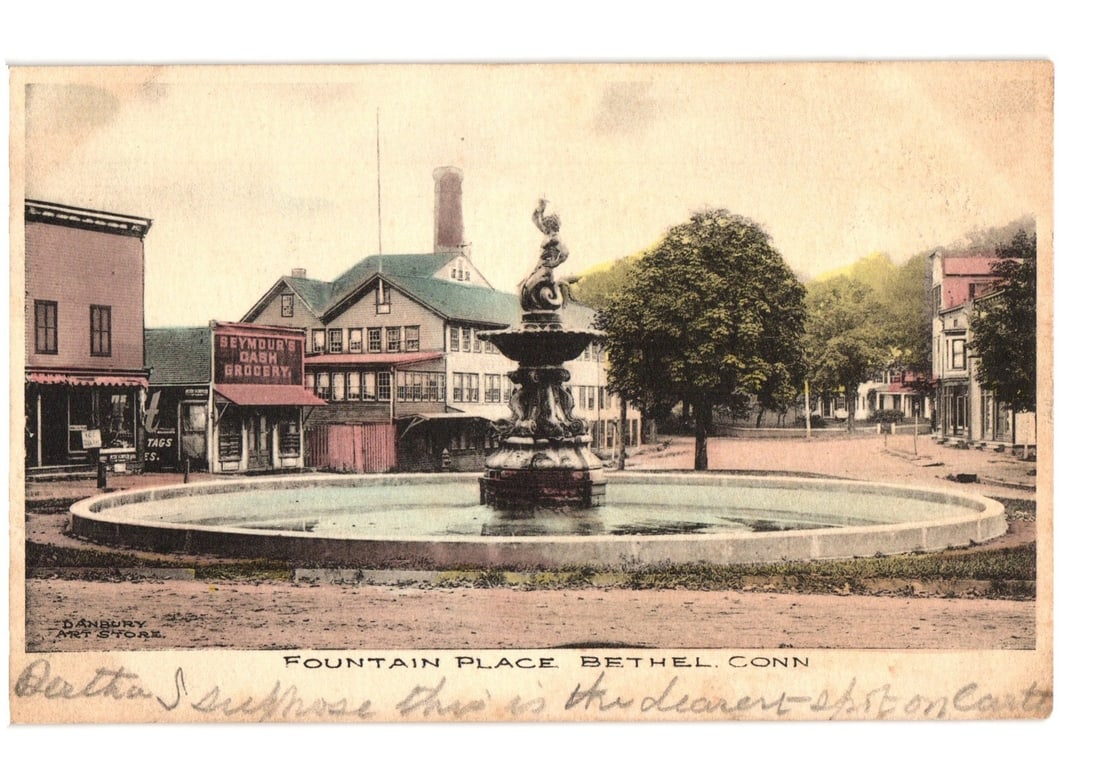 Fountain Place, Bethel, Conn., with Seymour's Grocery and town buildings, early 20th century: A central fountain featuring a classical statue, likely a cherub or putto, atop a multi-tiered basin, is the focal point of a town square. Surrounding buildings include a prominent structure marked 'S