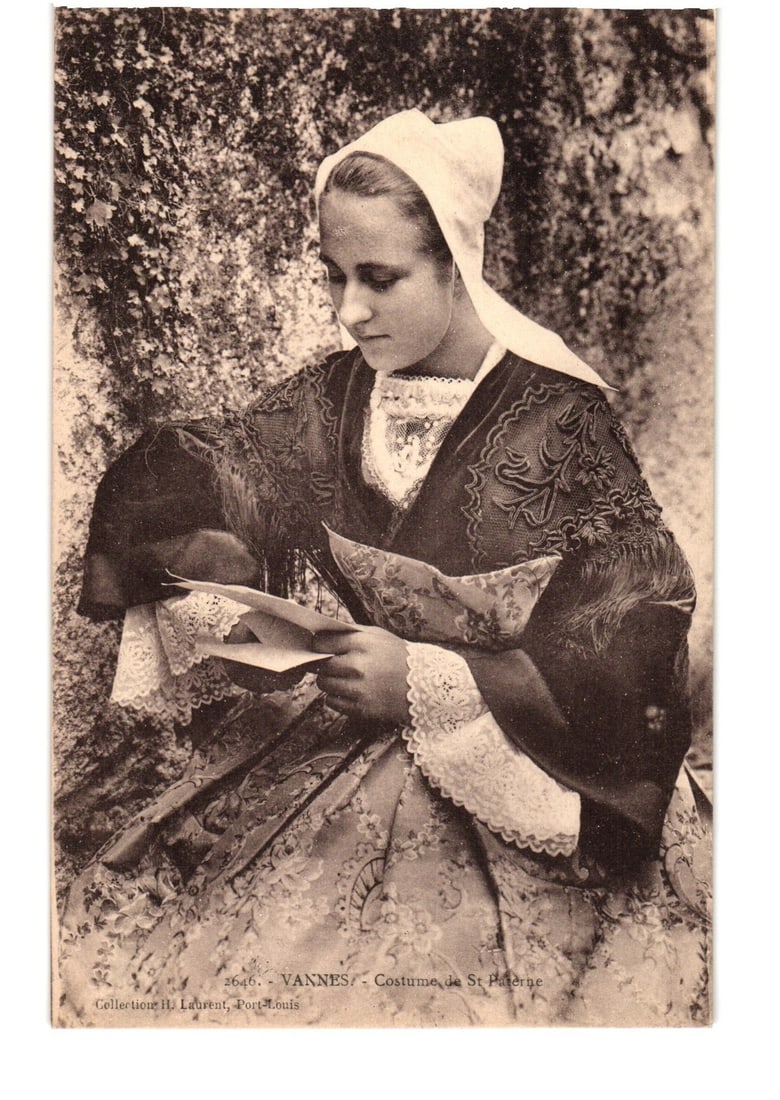 Early 20th Century Young Woman in Traditional St. Paterne Costume, Vannes, France Postcard: A young woman is depicted seated, looking down at a letter she holds in her hands. She is dressed in a traditional costume, featuring a white coiffe, an elaborately embroidered dark top with broad sle