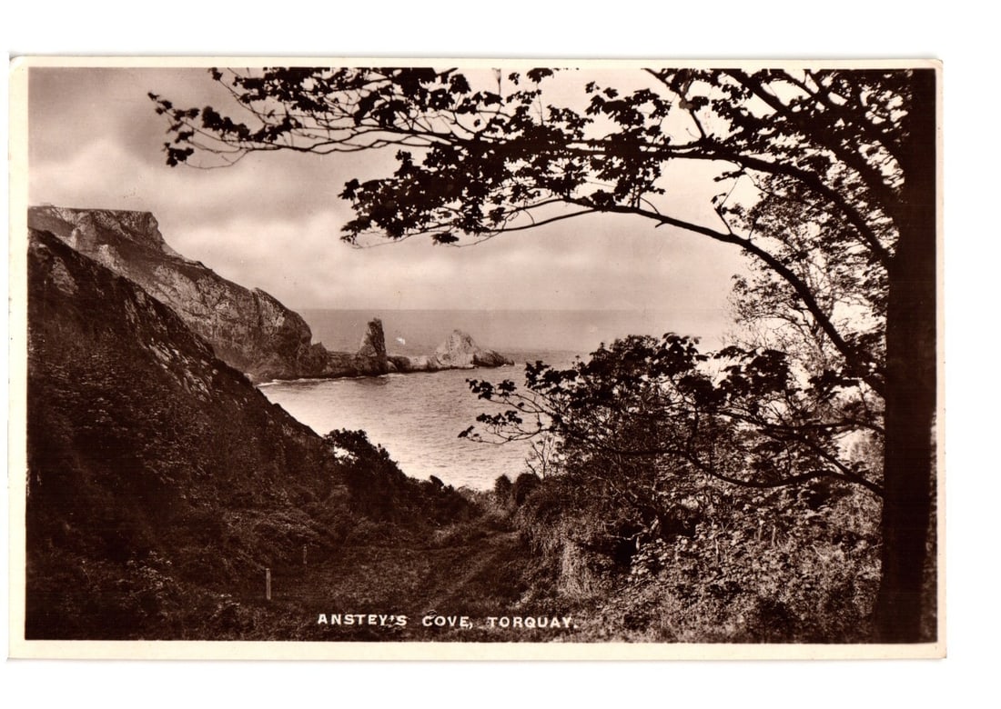 Early 20th Century Photographic Postcard of Anstey's Cove, Torquay, Coastal Landscape.: A sepia-toned photographic postcard depicts Anstey's Cove in Torquay, presenting a dramatic coastal landscape. Towering cliffs dominate the left side of the image, sloping steeply down towards the sea