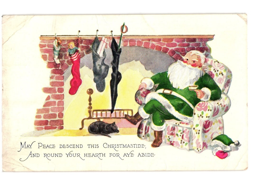 Illustrated Christmas Postcard: Santa Claus by Fireplace with Stockings, Black Cat, Early 20th C.: Santa Claus is depicted in a green fur-trimmed suit, seated in an ornate floral armchair to the right of a brick fireplace. He has a long white beard and a rosy complexion, holding a small white cup o