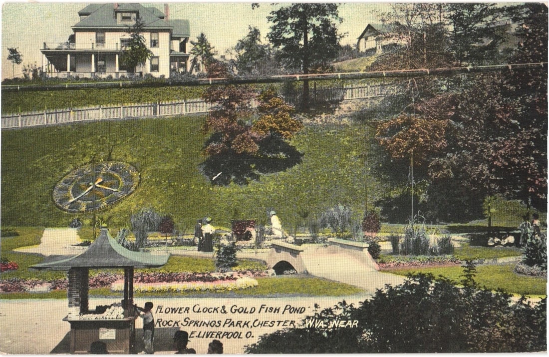 Landscape View of Flower Clock and Gold Fish Pond at Rock Springs Park, Chester, West Virginia: A landscaped park scene features a large flower clock on a grassy hillside, with prominent hands. Below, a gold fish pond is visible, crossed by a small stone bridge. Several figures are scattered; tw