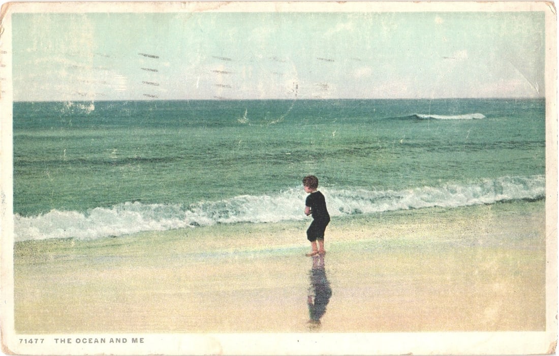 Coastal Scene Postcard: Young Child Wading in Ocean Waves on a Sandy Beach, c. 1920: A young child, dressed in dark clothing, stands at the edge of the water on a sandy beach. The child is positioned with their back mostly towards the viewer, facing out towards the vast ocean. Waves b