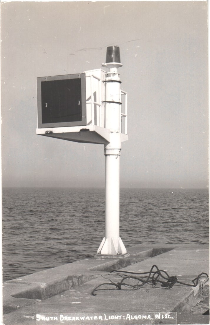 South Breakwater Light at Algoma, Wisconsin, a Nautical Navigation Aid, Real Photo postcard: A Real Photo Postcard in black and white captures the South Breakwater Light in Algoma, Wisconsin, rising prominently from a concrete breakwater extending into calm water. The light structure features