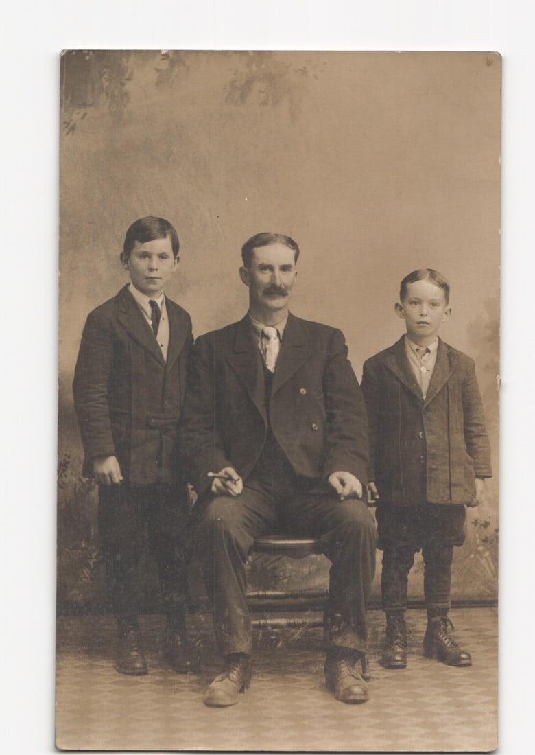 Early 20th century studio portrait postcard of a mustachioed man seated with two young boys.: Please review the photos carefully for additional condition details. Note that scans may appear slightly darker or lighter than the item's true appearance, and minor scanning artifacts may be visible.