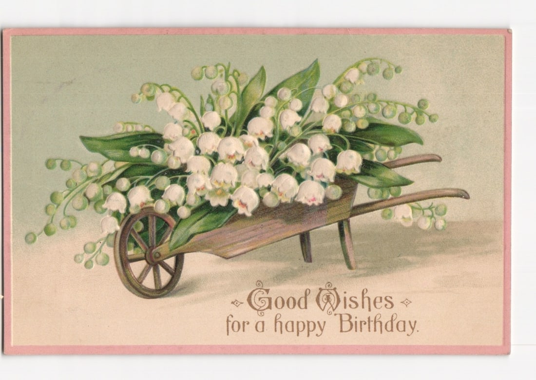 Early 20th Century Birthday Greetings Postcard with Lily of the Valley in a Wheelbarrow: A rustic wooden wheelbarrow, angled slightly, is centered, overflowing with a large bouquet of white lily of the valley flowers and green leaves. The background features a gradient from light green at